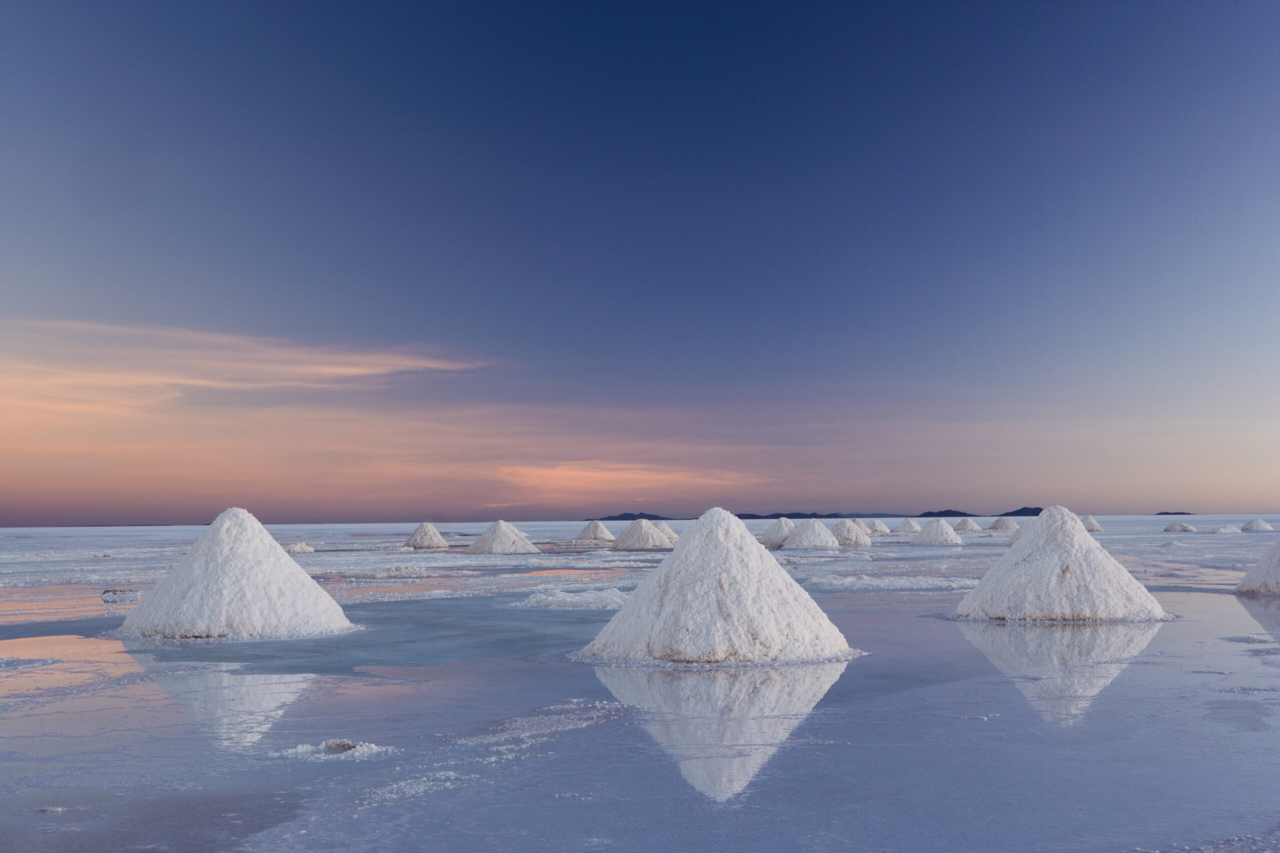 The salt pans of Salar de Uyuni, with shallow water and mineral deposits. White salt granules raked into heaps.